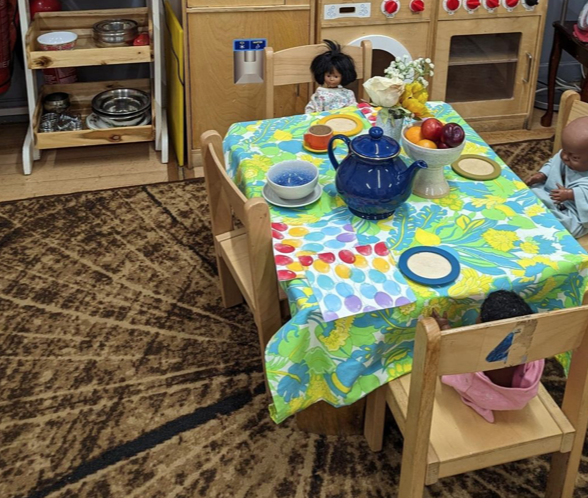 A table with a doll and a teapot on it
Description automatically generated