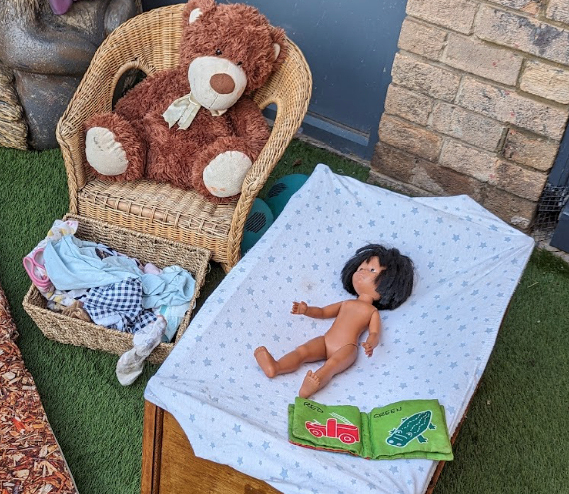 A doll on a bed next to a teddy bear
Description automatically generated