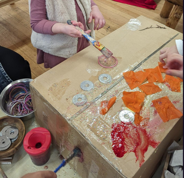 A group of kids painting on a cardboard box
Description automatically generated
